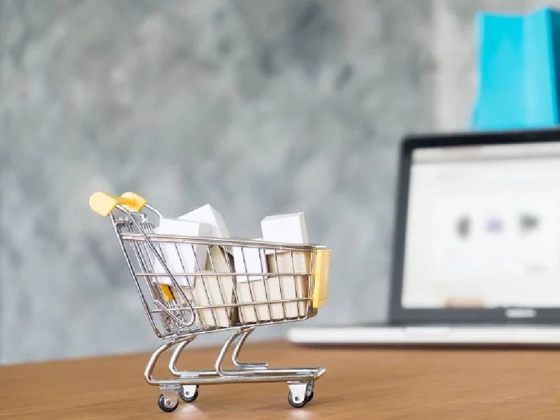 A mini shopping cart with parcels next to a laptop